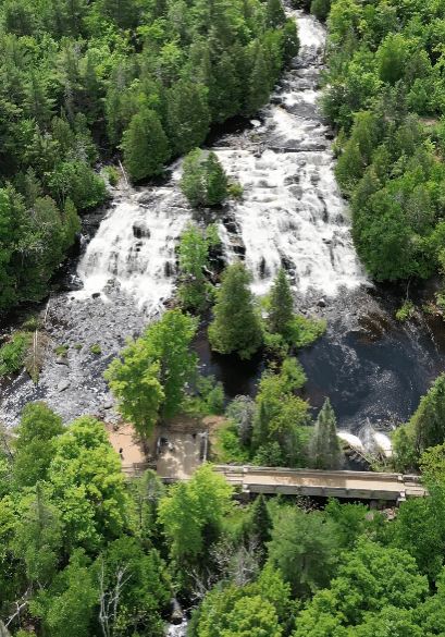 Aerial view of majestic waterfalls surrounded by dense green forest, with a road bridge gracefully crossing the river below.